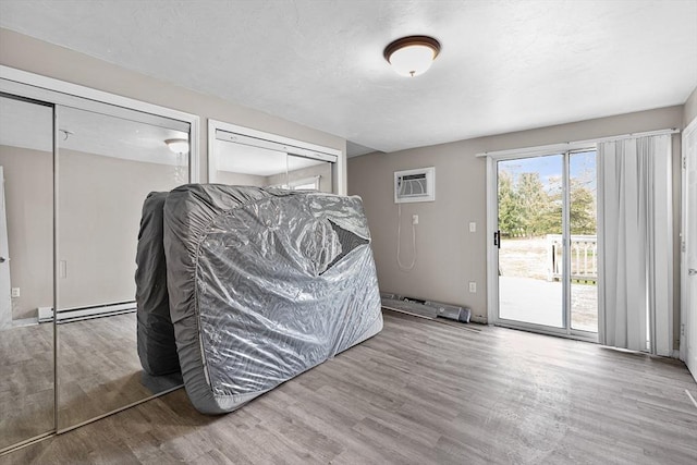 interior space with wood finished floors, a baseboard radiator, an AC wall unit, multiple closets, and access to outside