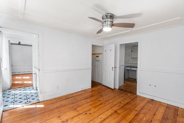 unfurnished bedroom featuring a baseboard radiator, a ceiling fan, hardwood / wood-style flooring, and connected bathroom