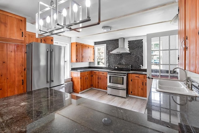 kitchen featuring a sink, appliances with stainless steel finishes, a healthy amount of sunlight, and wall chimney range hood