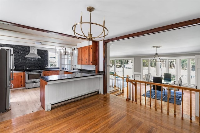kitchen featuring baseboard heating, wall chimney range hood, a chandelier, a sink, and appliances with stainless steel finishes