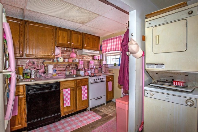 kitchen featuring stacked washer / drying machine, white electric range oven, black dishwasher, fridge, and a drop ceiling