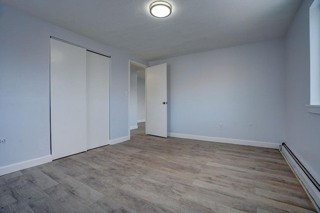 unfurnished bedroom with baseboard heating, a closet, and light hardwood / wood-style flooring