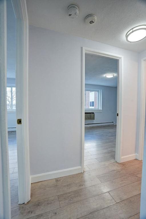 corridor featuring a baseboard radiator, light hardwood / wood-style flooring, and a textured ceiling