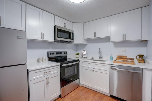 kitchen with appliances with stainless steel finishes, white cabinetry, sink, a textured ceiling, and light hardwood / wood-style flooring