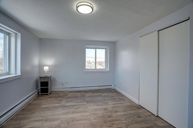 unfurnished bedroom featuring a baseboard heating unit, a closet, and light wood-type flooring