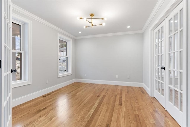 spare room featuring a notable chandelier, light hardwood / wood-style flooring, crown molding, and french doors