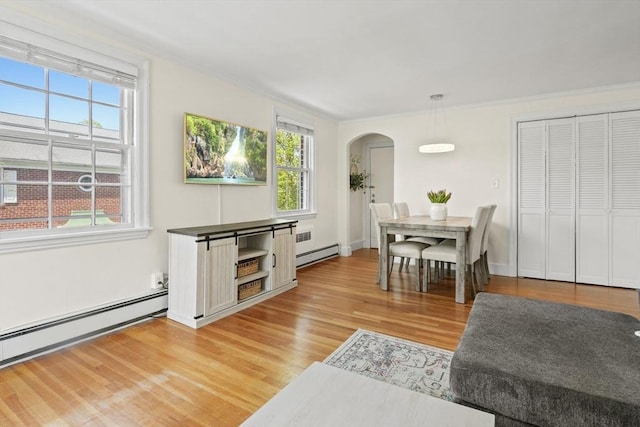 dining area featuring crown molding, arched walkways, baseboard heating, and light wood finished floors