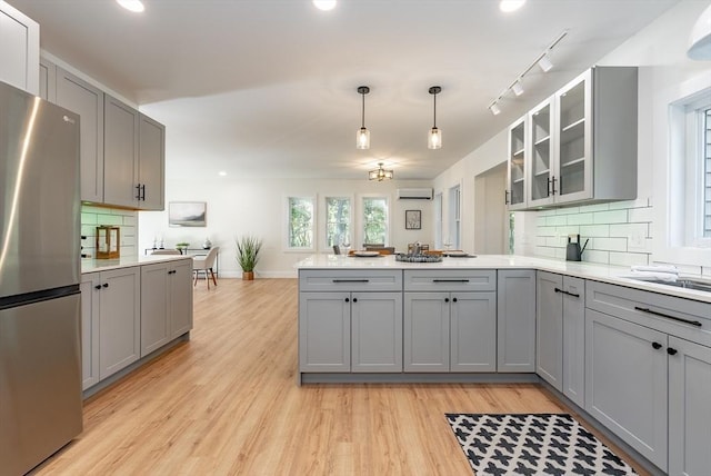 kitchen with freestanding refrigerator, a peninsula, a wall mounted air conditioner, light wood finished floors, and gray cabinetry