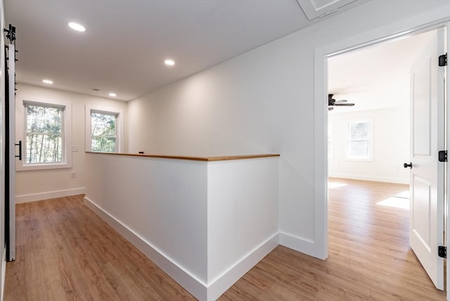 corridor with baseboards, light wood finished floors, a healthy amount of sunlight, and an upstairs landing