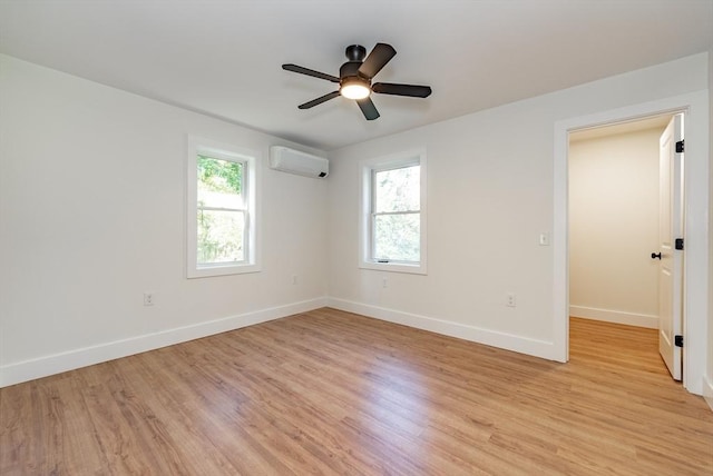 spare room featuring an AC wall unit, baseboards, a ceiling fan, and light wood-style flooring
