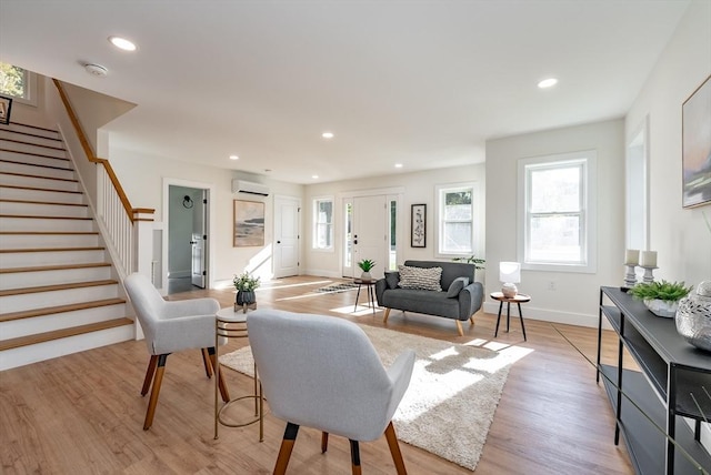 living room featuring a wall unit AC, stairway, baseboards, light wood finished floors, and recessed lighting