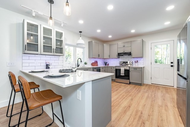 kitchen featuring gray cabinets, a peninsula, a kitchen bar, and stainless steel appliances