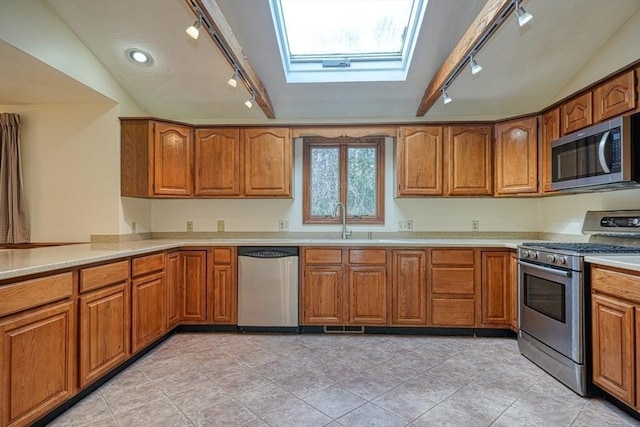 kitchen featuring vaulted ceiling with skylight, appliances with stainless steel finishes, brown cabinetry, and a sink