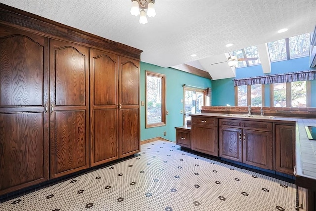 kitchen with a textured ceiling, dark brown cabinetry, vaulted ceiling, ceiling fan, and sink