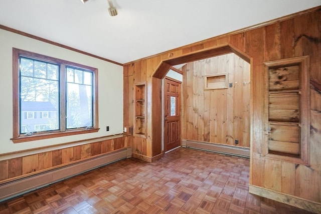 spare room with a baseboard radiator, crown molding, parquet floors, and wooden walls