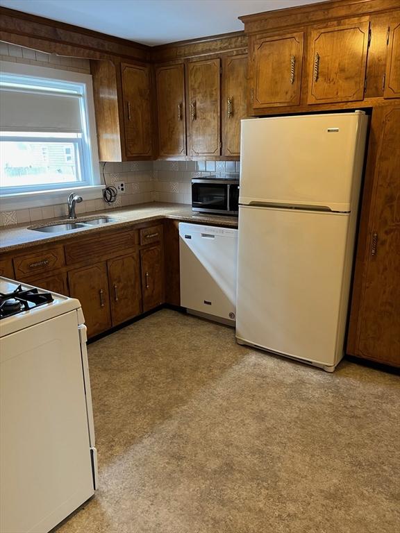 kitchen with white appliances, backsplash, light floors, and a sink