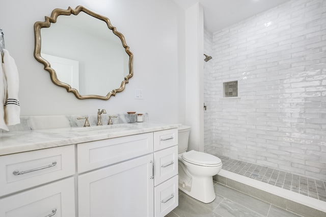 bathroom with toilet, tile floors, vanity, and tiled shower