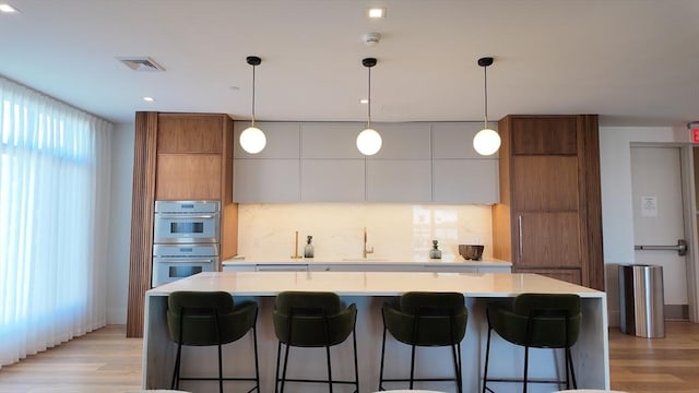 191 Washington St Unit 309, Boston, MA 02135 - kitchen featuring modern cabinets, brown cabinets, double oven, light wood-type flooring, and decorative backsplash