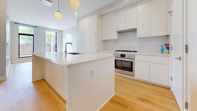 191 Washington St Unit 309, Boston, MA 02135 - kitchen featuring oven, a sink, under cabinet range hood, backsplash, and white cabinets