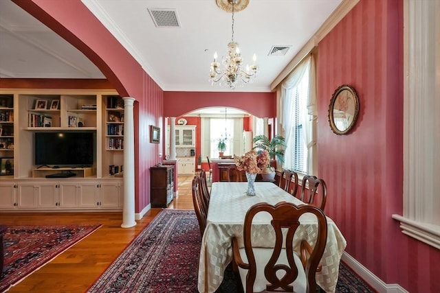 dining space with crown molding, light hardwood / wood-style flooring, built in shelves, a chandelier, and decorative columns