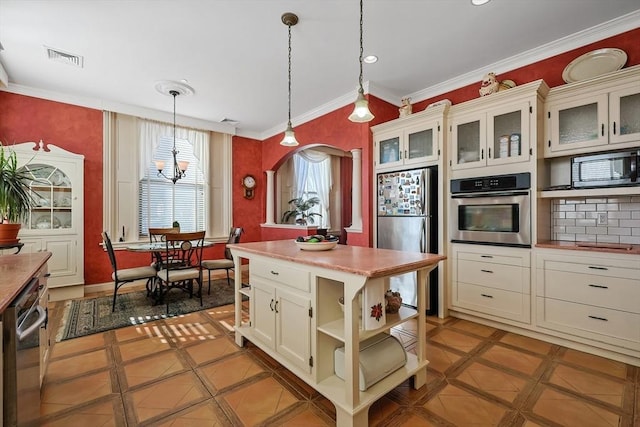 kitchen featuring a notable chandelier, a kitchen island, hanging light fixtures, appliances with stainless steel finishes, and ornamental molding