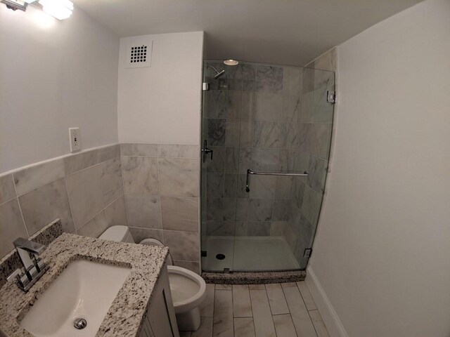 full bathroom featuring visible vents, tile walls, a shower stall, vanity, and toilet