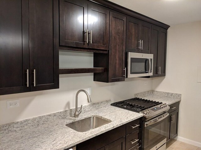 kitchen featuring open shelves, appliances with stainless steel finishes, dark brown cabinetry, a sink, and light stone counters