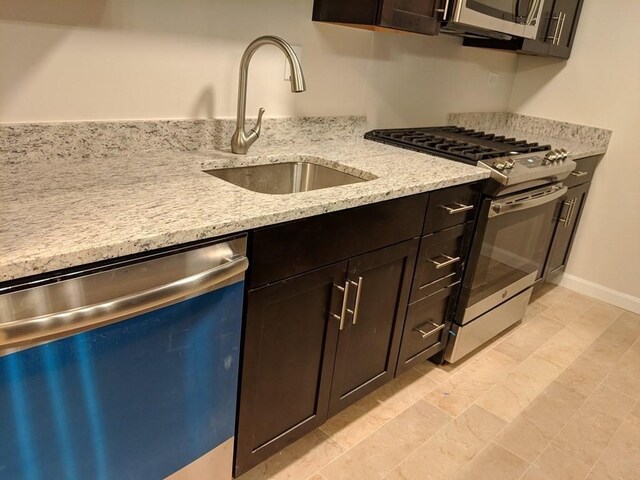 kitchen with stainless steel appliances, dark brown cabinetry, light stone counters, and a sink