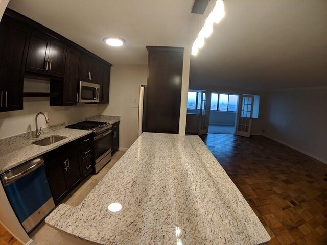 kitchen with light stone countertops, a sink, stainless steel appliances, baseboards, and open floor plan