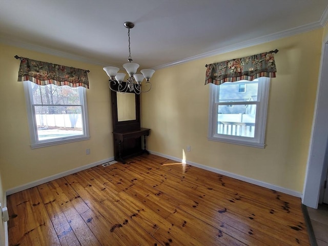 unfurnished dining area with a chandelier, crown molding, baseboards, and hardwood / wood-style flooring