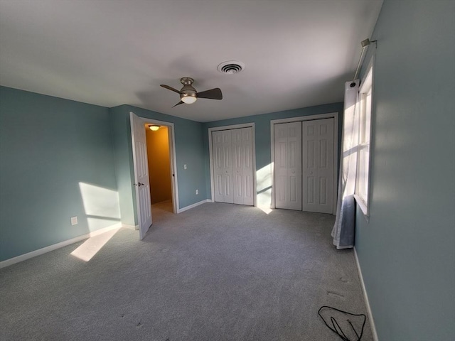 unfurnished bedroom with carpet floors, multiple closets, visible vents, a ceiling fan, and baseboards