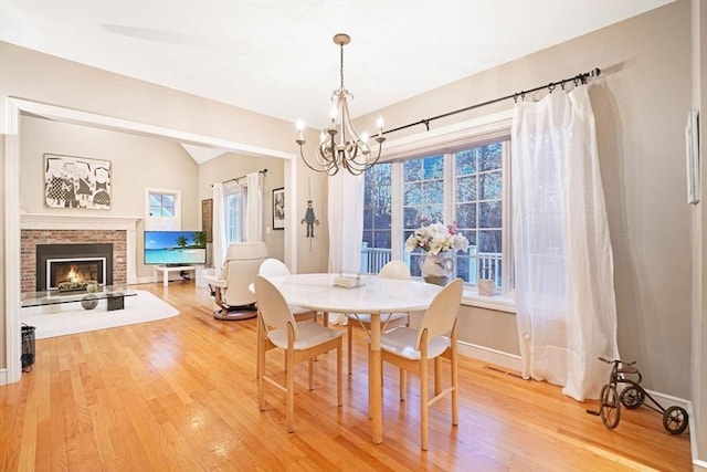 dining space featuring a healthy amount of sunlight, light wood-style flooring, a fireplace, and a notable chandelier