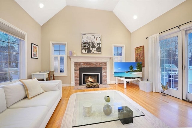 living room featuring high vaulted ceiling, a fireplace, wood finished floors, and baseboards