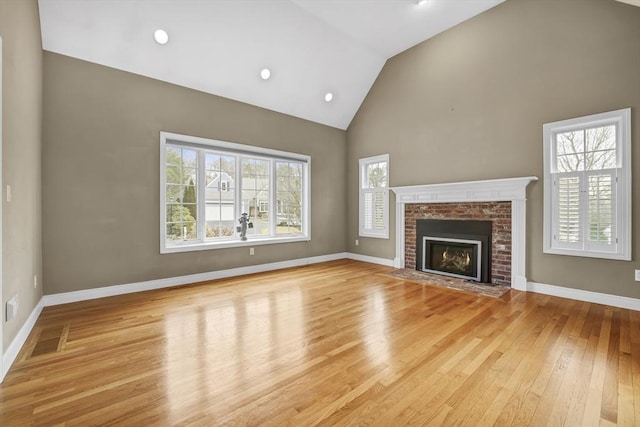 unfurnished living room featuring high vaulted ceiling, a brick fireplace, baseboards, and wood finished floors