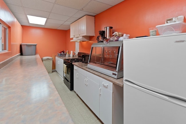 kitchen featuring a paneled ceiling, white fridge, black range with gas cooktop, and white cabinetry