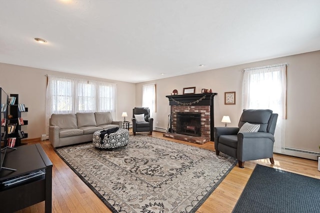 living room featuring baseboard heating, light wood-type flooring, and a brick fireplace