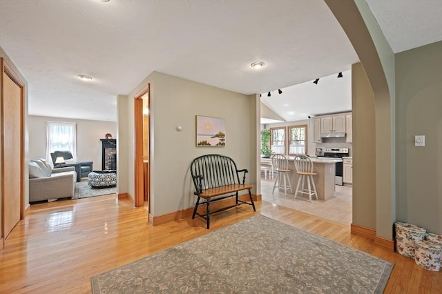 hall featuring arched walkways, light wood finished floors, and baseboards