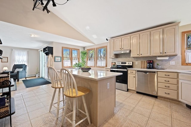 kitchen featuring stainless steel appliances, under cabinet range hood, cream cabinets, lofted ceiling, and a baseboard radiator