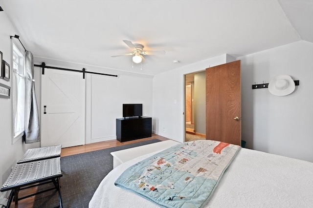 bedroom with a barn door, a ceiling fan, and wood finished floors