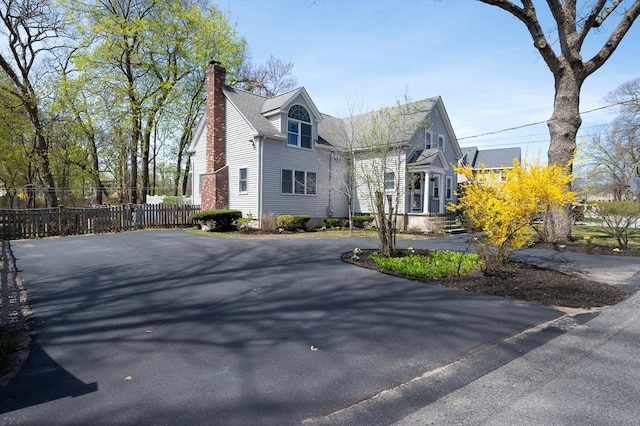 view of side of home with a chimney, fence, and driveway