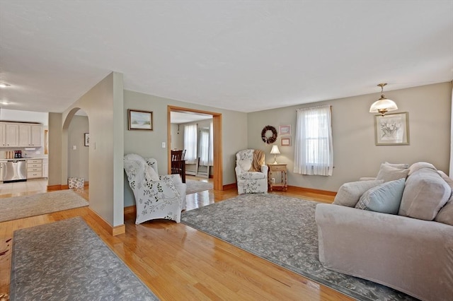 living room with arched walkways, light wood-style floors, a baseboard heating unit, and baseboards