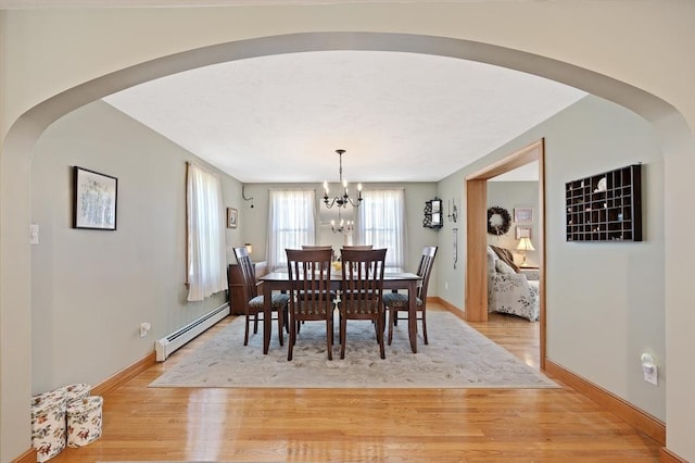 dining room featuring baseboard heating, arched walkways, light wood-type flooring, a chandelier, and baseboards