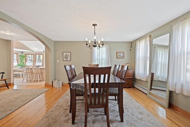 dining area with arched walkways, light wood finished floors, a chandelier, baseboards, and a baseboard heating unit