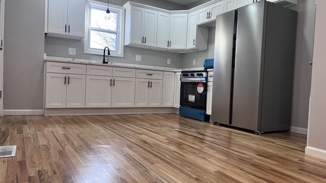 kitchen with pendant lighting, appliances with stainless steel finishes, white cabinetry, light hardwood / wood-style floors, and sink