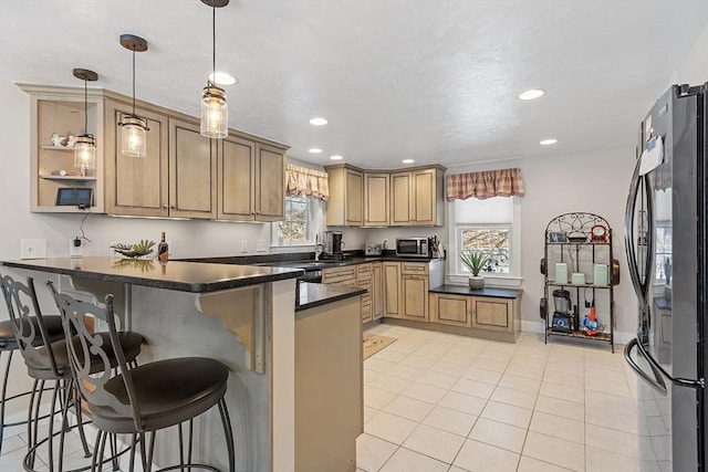 kitchen with dark countertops, stainless steel microwave, a breakfast bar, freestanding refrigerator, and a peninsula