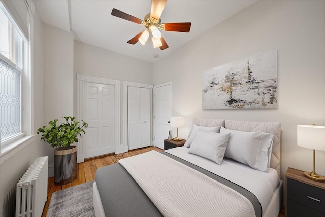 bedroom featuring radiator heating unit, two closets, wood finished floors, and a ceiling fan