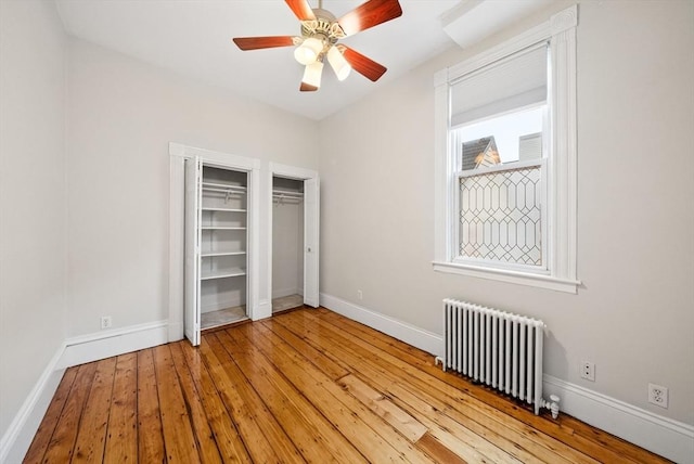 unfurnished bedroom with radiator heating unit, hardwood / wood-style floors, baseboards, and ceiling fan