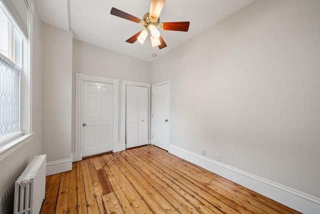unfurnished bedroom with radiator, two closets, baseboards, light wood-style flooring, and a ceiling fan