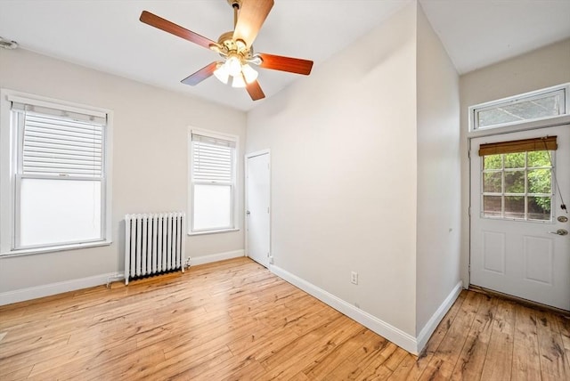 spare room featuring radiator heating unit, light wood-type flooring, baseboards, and a ceiling fan
