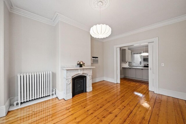 unfurnished living room with radiator heating unit, crown molding, baseboards, light wood-style flooring, and a fireplace